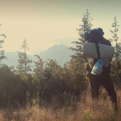 Photo by Tamás Mészáros A lone hiker with a backpack and sleeping mat in a sunny mountain landscape.