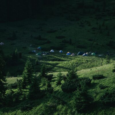 A peaceful camping site nestled in the lush green mountains of Romania, showcasing tents and nature's beauty.