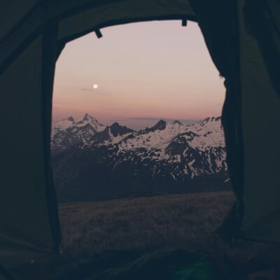 Capture of a breathtaking sunset view over snowy mountains from inside a tent, perfect for adventure seekers.