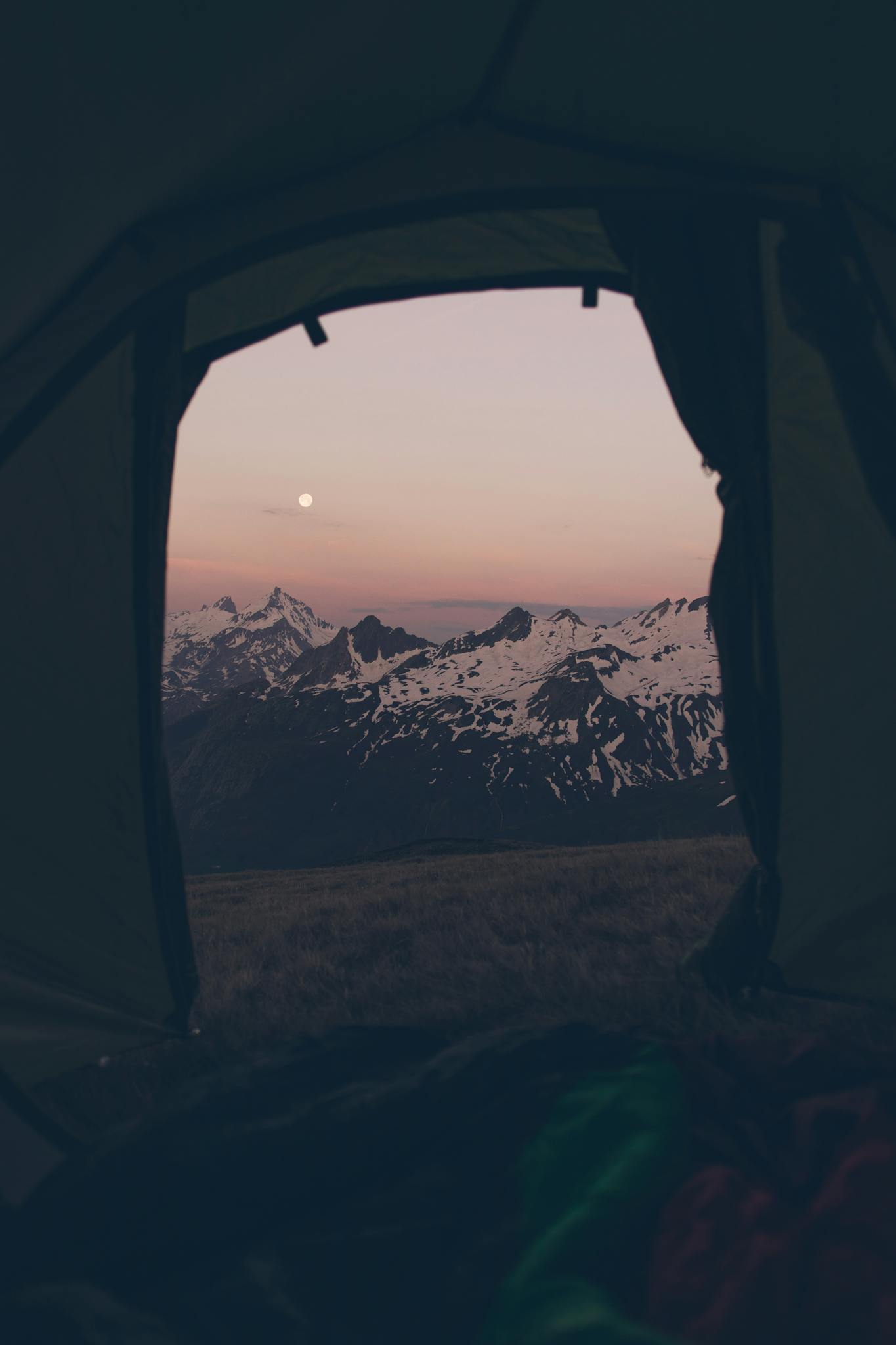 Capture of a breathtaking sunset view over snowy mountains from inside a tent, perfect for adventure seekers.